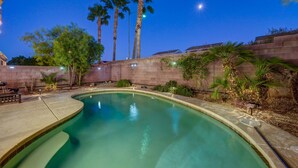 A swimming pool with a curved edge, surrounded by palm trees and a stone wall. - Luxe 3 Bedroom Home with optional Heated Pool 🌊 6Mi to LV Strip!💫✨ (Las Vegas)