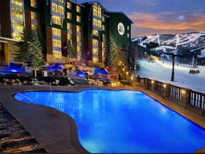 Un hotel con piscina, mobiliario exterior y vistas a una cadena montañosa nevada.