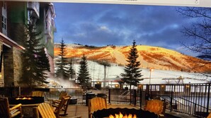 Un espace extérieur accueillant, aménagé avec des sièges confortables et un foyer circulaire entouré de chaises en bois, offrant une vue panoramique sur les montagnes.