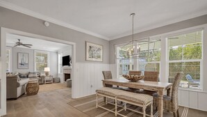 A spacious living room with a dining area, a fireplace, and large windows. - Amazing Island Oasis, Heated Pool, Outdoor Bar Area with TV, Bocce Ball Court & Putting Green (Saint Simons Island)