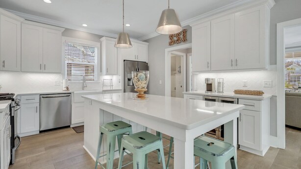 A modern kitchen with white cabinets, a central island with stools, pendant lighting, and stainless steel appliances. - Amazing Island Oasis, Heated Pool, Outdoor Bar Area with TV, Bocce Ball Court & Putting Green (Saint Simons Island)