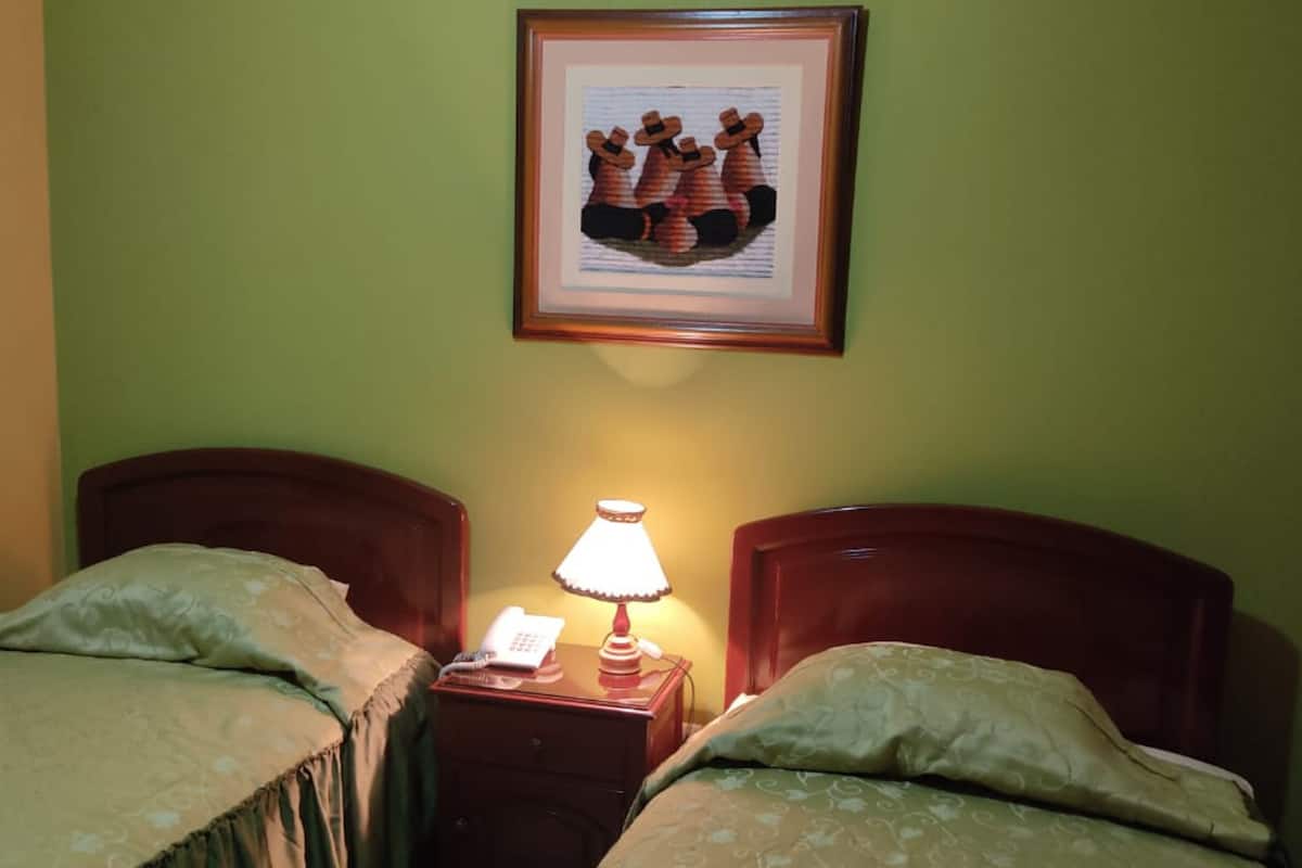 Une chambre avec deux lits, une table de chevet avec une lampe et un tableau encadré au mur.
