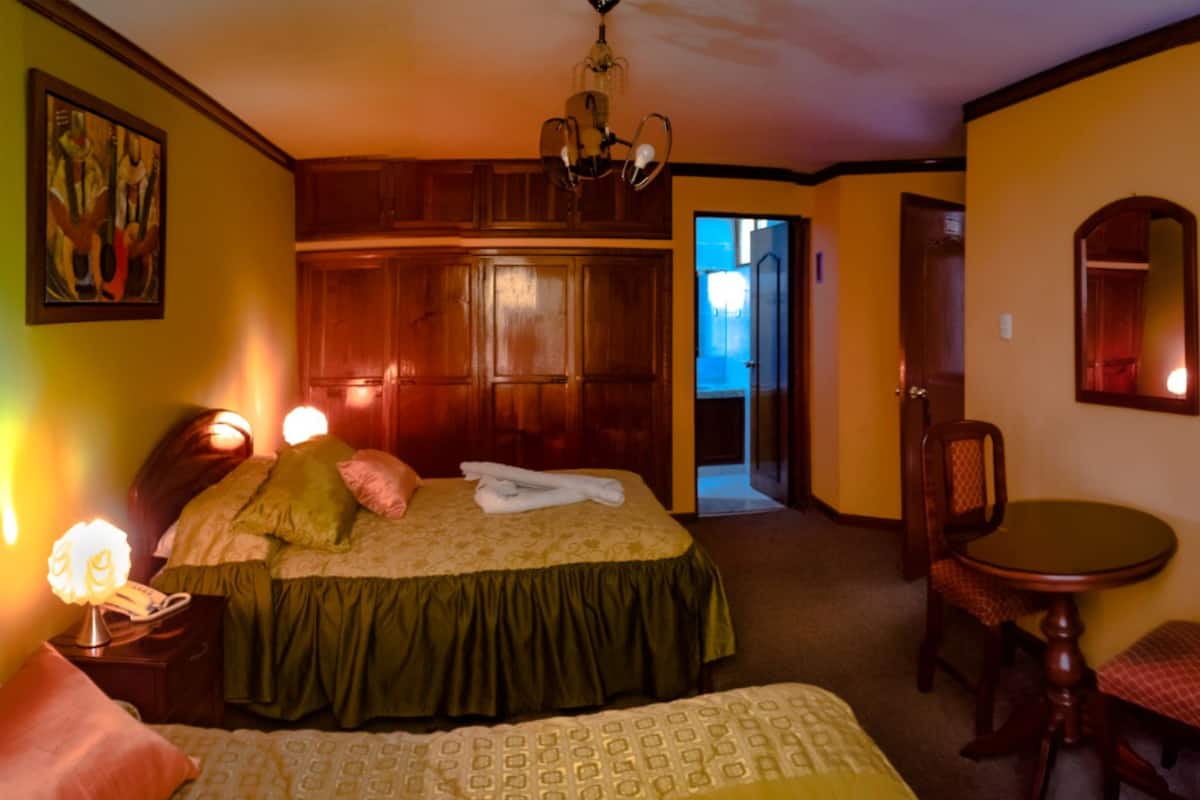 Une chambre d’hôtel avec deux lits, une armoire en bois, une table à manger avec une chaise et un miroir au mur.