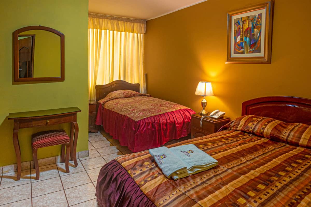 Une chambre d’hôtel avec un lit, un bureau, une chaise, une table de chevet avec une lampe et un tableau au mur.