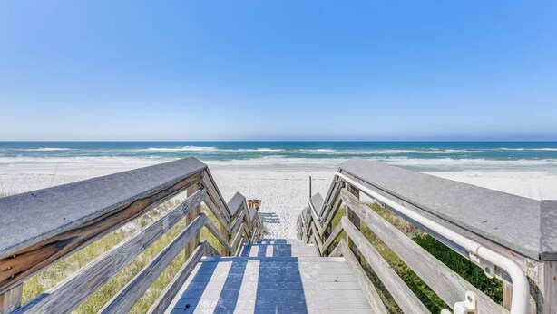Ein Holzsteg führt zu einem Strand mit freiem Blick auf den Ozean.