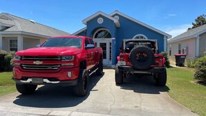 En rød Chevrolet pickup og en rød ATV parkeret foran et blåt hus med en hvid dør.