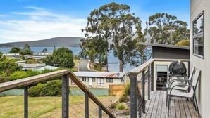 Une terrasse en bois avec une rambarde, un barbecue et une vue sur un lac et des collines.