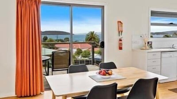 Un espace repas comprenant une table, des chaises et une vue sur la mer grâce à de grandes fenêtres.