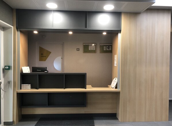 Un comptoir d’accueil équipé d’un ordinateur, d’une caisse enregistreuse et d’un petit présentoir. Des panneaux indiquent les services proposés et les tarifs.