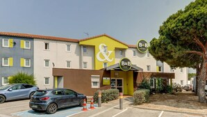 Ein Bed & Breakfast Hotel mit gelb-brauner Fassade, einem Parkplatz mit Autos und einem Baum rechts.