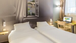 Ein Hotelzimmer mit zwei Betten, einem Schreibtisch mit einem Laptop, einem Fenster mit Blick auf eine Brücke über einem Fluss und einem Vorhang.