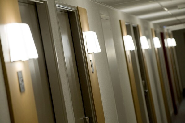 Ein Hotelgang mit Türen, über jeder Tür eine Lampe.