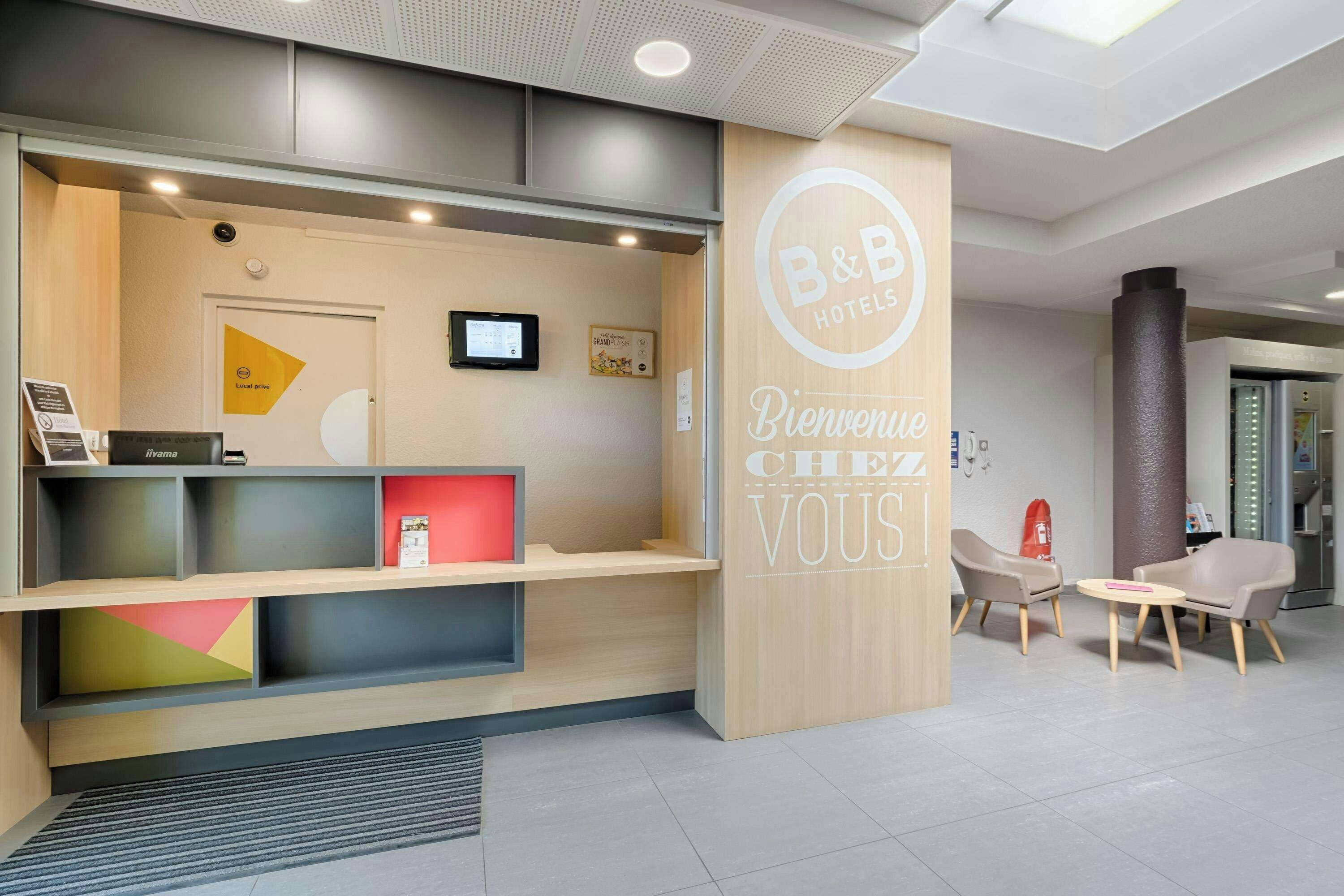 Ein Hotel-Empfangsbereich mit modernem Design, inklusive einer Rezeption, einer Sitzecke und einem digitalen Bildschirm.