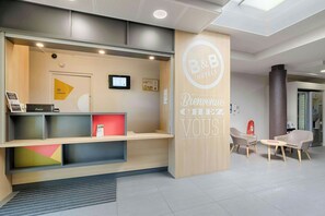 A hotel reception area with a modern design, including a reception desk, seating area, and a digital screen.