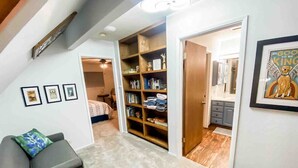 Una habitación pequeña con un sillón gris, una estantería y un cuadro en la pared.