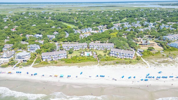 An aerial view of a coastal residential area with beachfront properties, including houses and a hotel with multiple buildings and a pool.