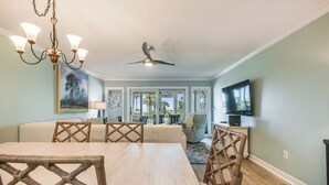 A dining area with a wooden table and chairs, a ceiling fan, and a television on the wall.