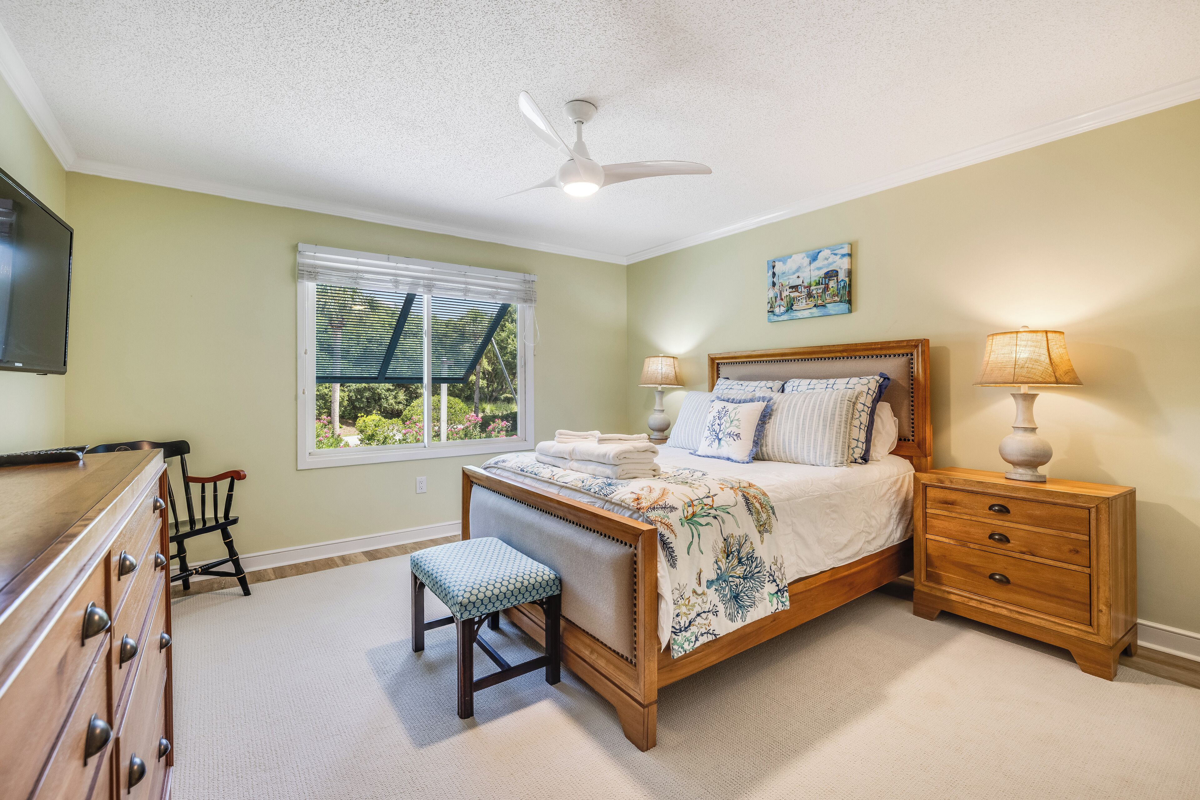 A bedroom with a bed, bedside tables, a chair, a dresser, and a ceiling fan.