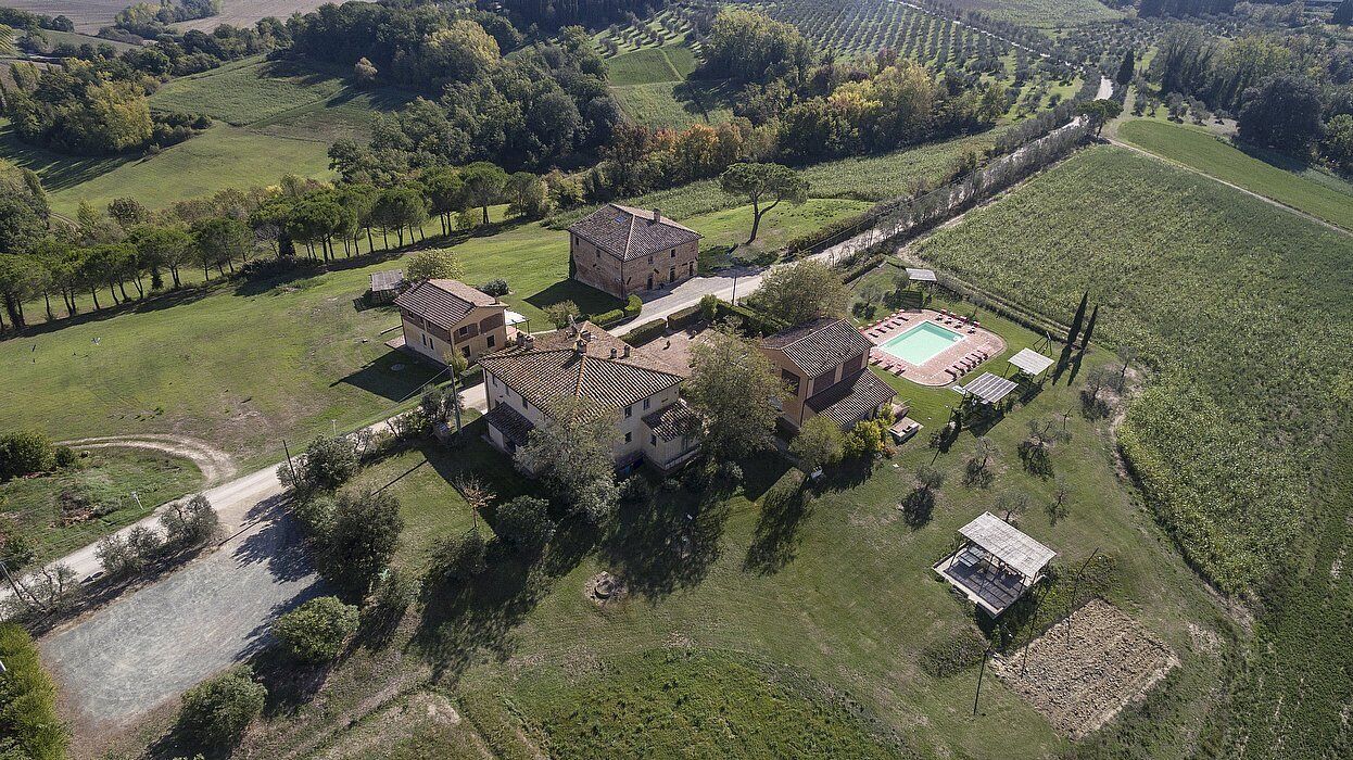 Vista aérea de una propiedad con un edificio central, una piscina y campos verdes circundantes.