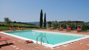 Ein rechteckiger Swimmingpool mit klarem, blauem Wasser, umgeben von roten Liegestühlen und einer überdachten Sitzgruppe.