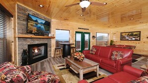 A cozy log cabin interior with a fireplace, red leather sofa, and a television mounted on a stone wall. - Private Poolside Bliss & Mountain Views! - A Splash of Heaven (Sevierville)