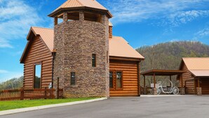 A log cabin with a stone tower, wooden exterior, and a covered porch with a wooden bench. - Private Poolside Bliss & Mountain Views! - A Splash of Heaven (Sevierville)