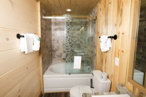 A wooden-paneled bathroom with a glass-enclosed shower, a white bathtub, and a toilet.