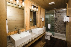 A wooden bathroom with two sinks, a toilet, and a glass shower enclosure. - Skyriver Falls - Luxury Indoor Pool, Mini Golf, Firepit, Mountain Views, Hot Tub + Game Room (Sevierville)