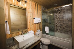 A wooden bathroom with a sink, toilet, and glass-enclosed shower.