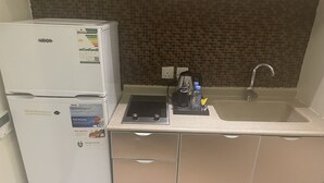 Pieni, käytännöllinen keittiö, jossa on valkoinen jääkaappi, musta kahvinkeitin ja hana, jossa on pesuallas.