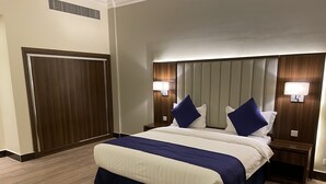 Hotellihuone, jossa on suuri sänky, kaksi yöpöytää, sängynpääty, jossa on sisäänrakennettu valaistus, ja puinen vaatekaappi.