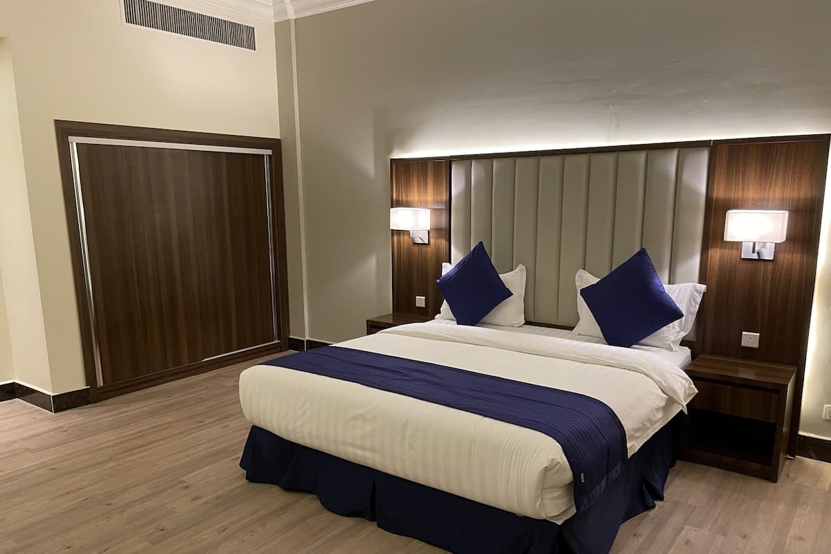 Une chambre d’hôtel avec un grand lit, deux tables de chevet, une tête de lit dotée d’un éclairage intégré et une armoire en bois.