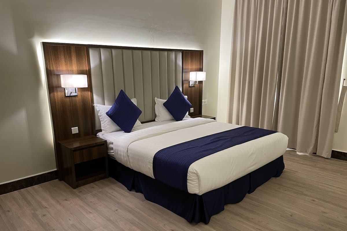 Une chambre d’hôtel avec un grand lit, deux tables de chevet, une tête de lit dotée d’un éclairage intégré et un rideau à la fenêtre.