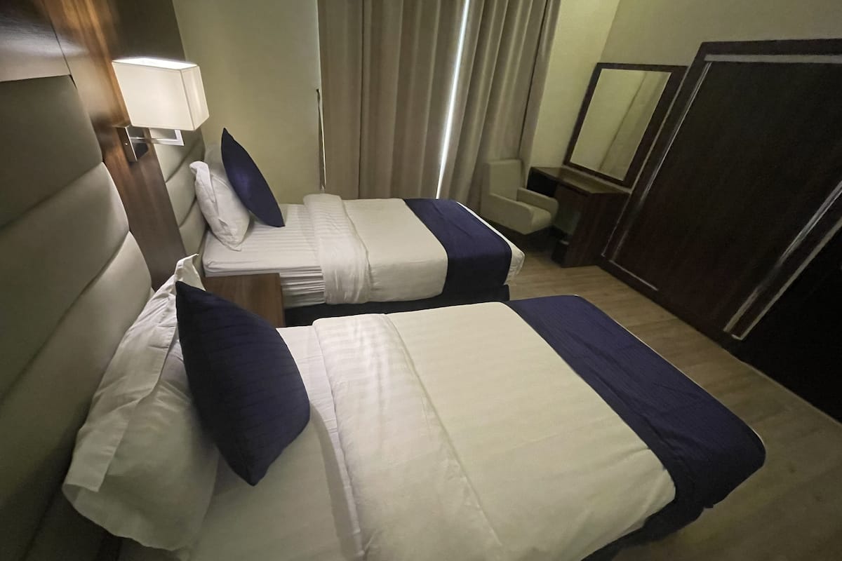 Une chambre d’hôtel avec deux lits, un bureau, une chaise, un miroir et une fenêtre avec des rideaux.