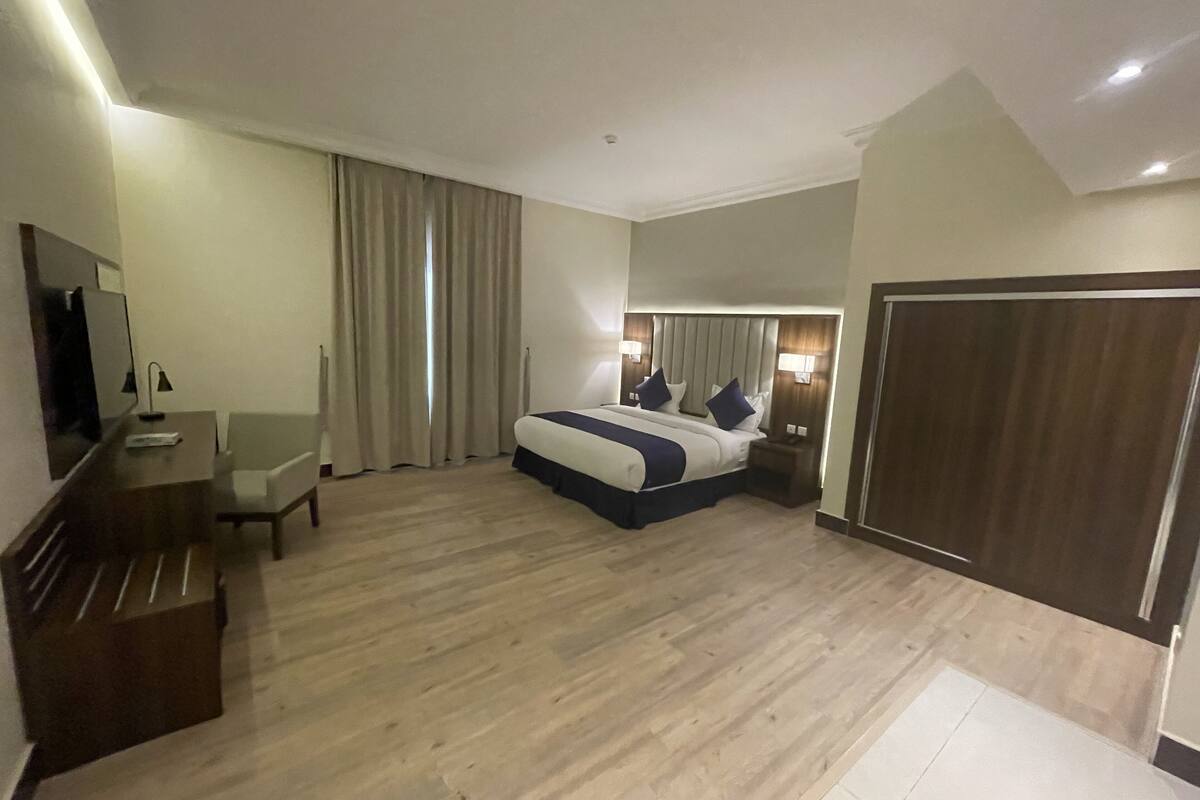 Une chambre d’hôtel avec un grand lit, un bureau avec une chaise, une télévision et une armoire.