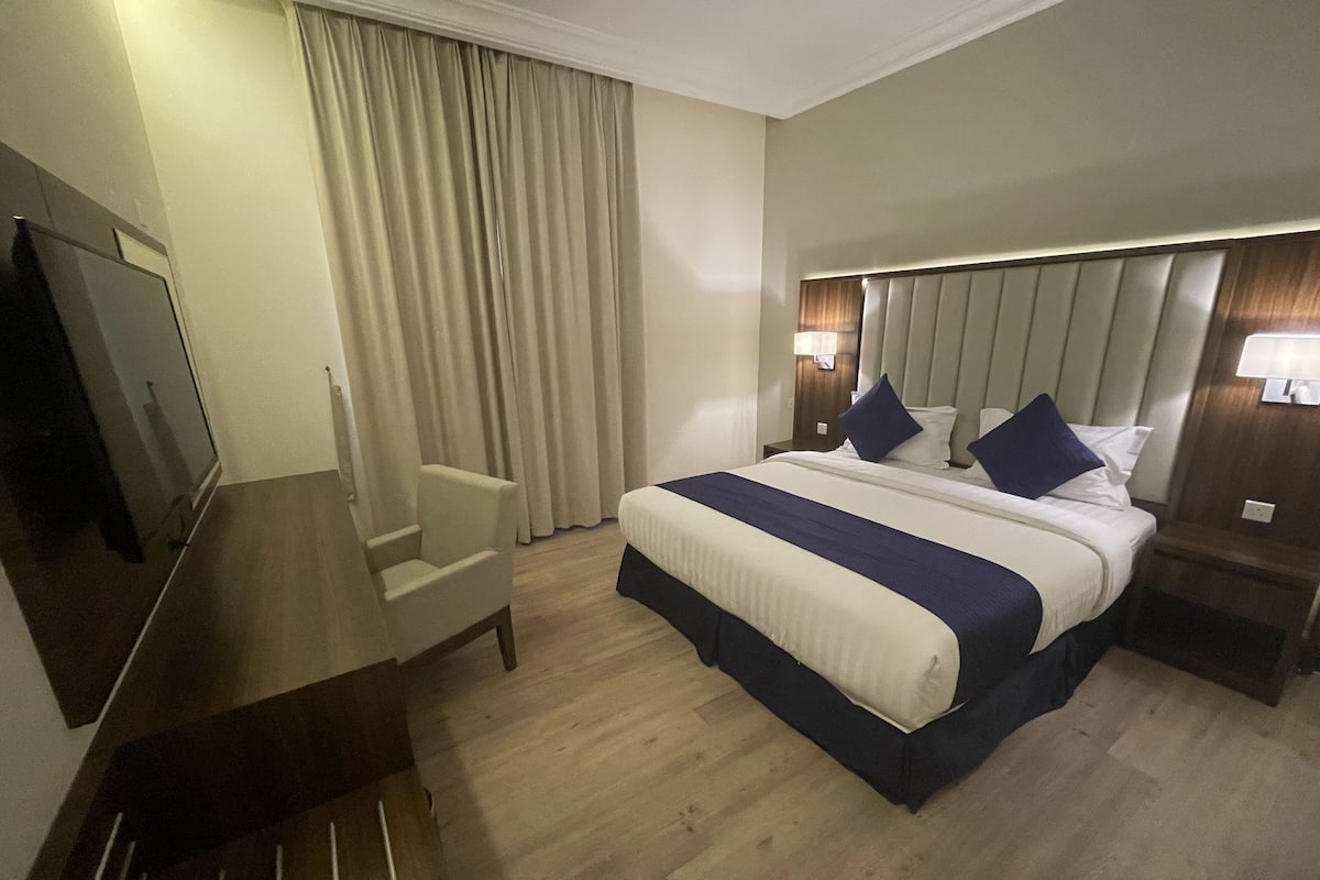 Une chambre d’hôtel avec un lit, une chaise, une télévision et des rideaux.