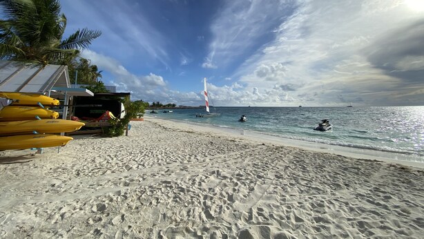 A beach with a clear sky, a sailboat, and yellow kayaks. - Lagoona Sunset (Maafushi)