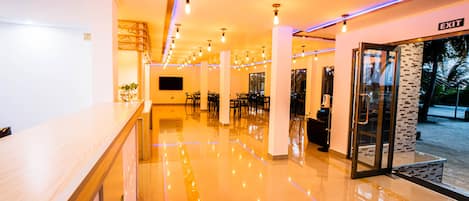 A hotel lobby with a polished floor, a reception desk, and a glass door leading outside.
