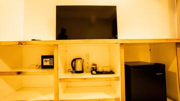 Una kitchenette compacta con un refrigerador negro, una cafetera y un hervidor sobre un estante de madera.