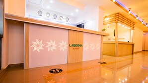 A hotel reception area with a wooden reception desk, a digital clock displaying time from various cities, and a sign reading "LAGOONA sunset." - Lagoona Sunset (Maafushi)