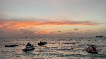 Atardecer sobre un mar tranquilo con varias embarcaciones y un jet ski.