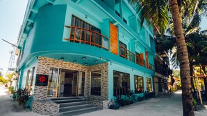 A two-story building with a turquoise facade, large windows, and a visible entrance with steps. - Lagoona Sunset (Maafushi)