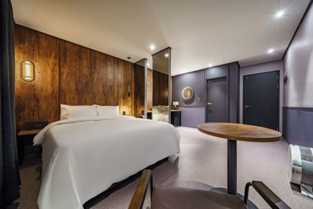 A modern hotel room with a large bed, a round wooden table, and a mirror.