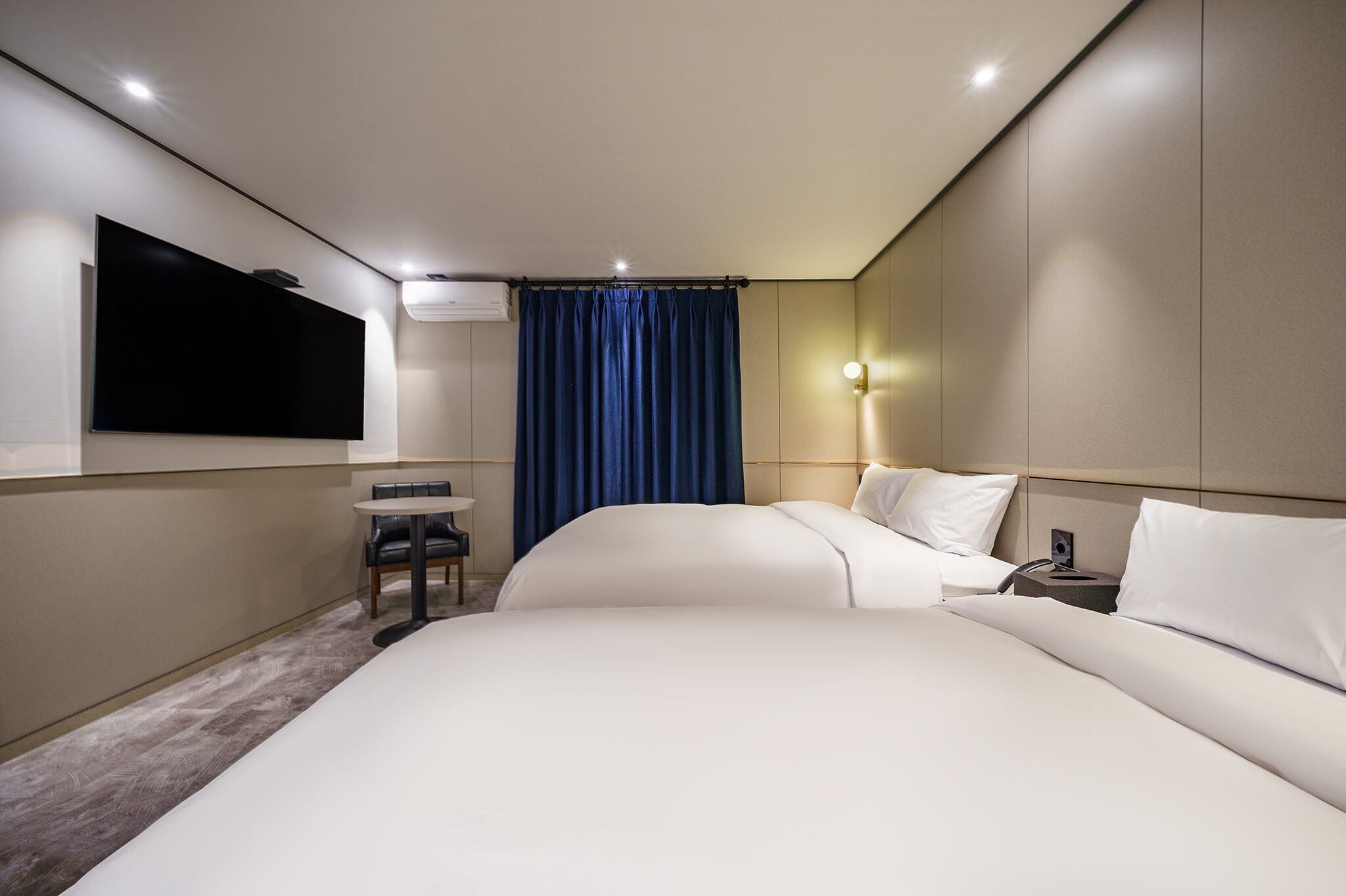 A modern hotel room with a large bed, a desk, and a flat-screen TV mounted on the wall.