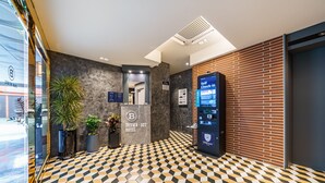 Ein Hotel-Empfangsbereich mit Check-in-Kiosk, einer Selbstbedienungsmaschine und einem gemusterten Boden.
