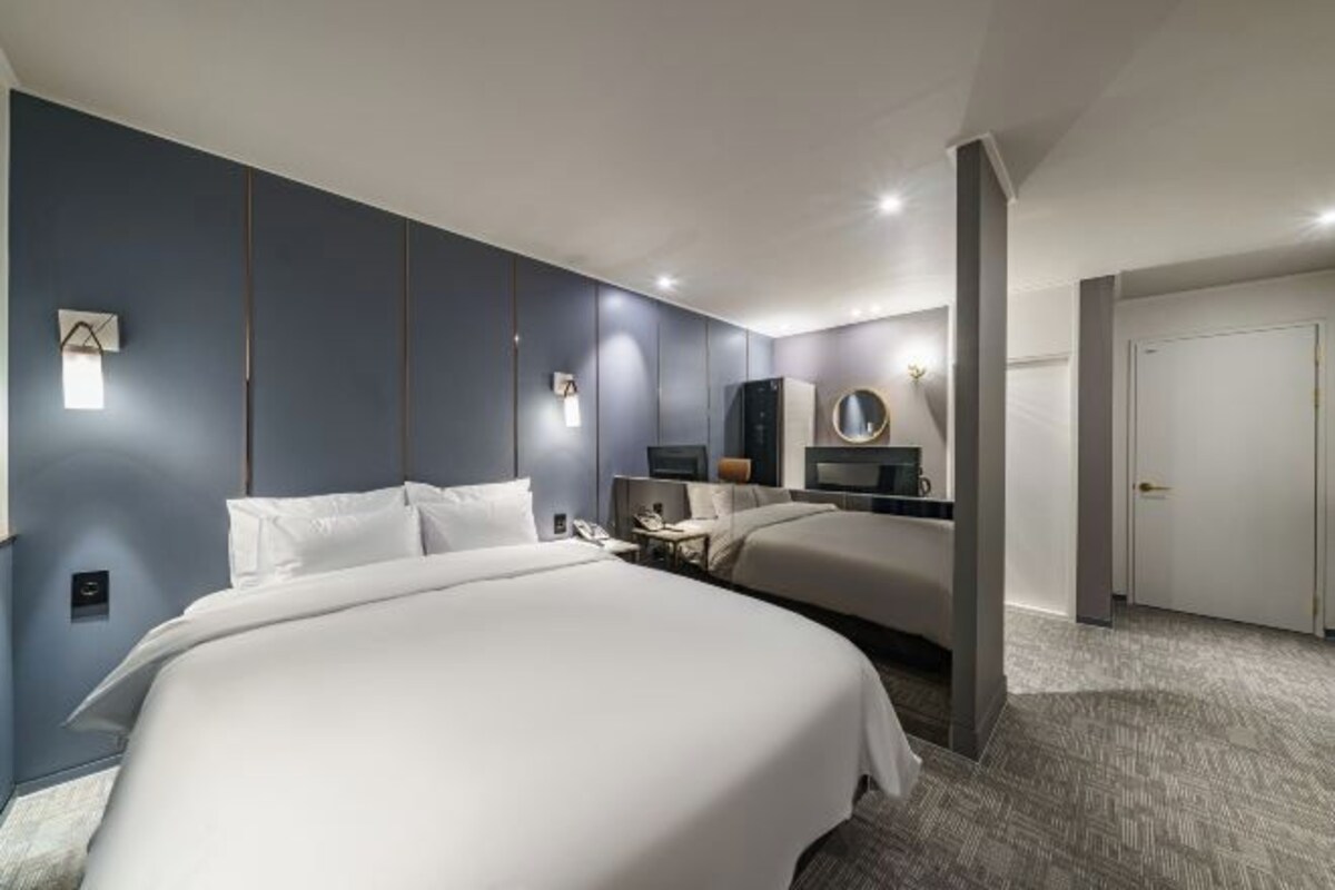 A modern hotel room with two beds, a desk, and a bathroom.