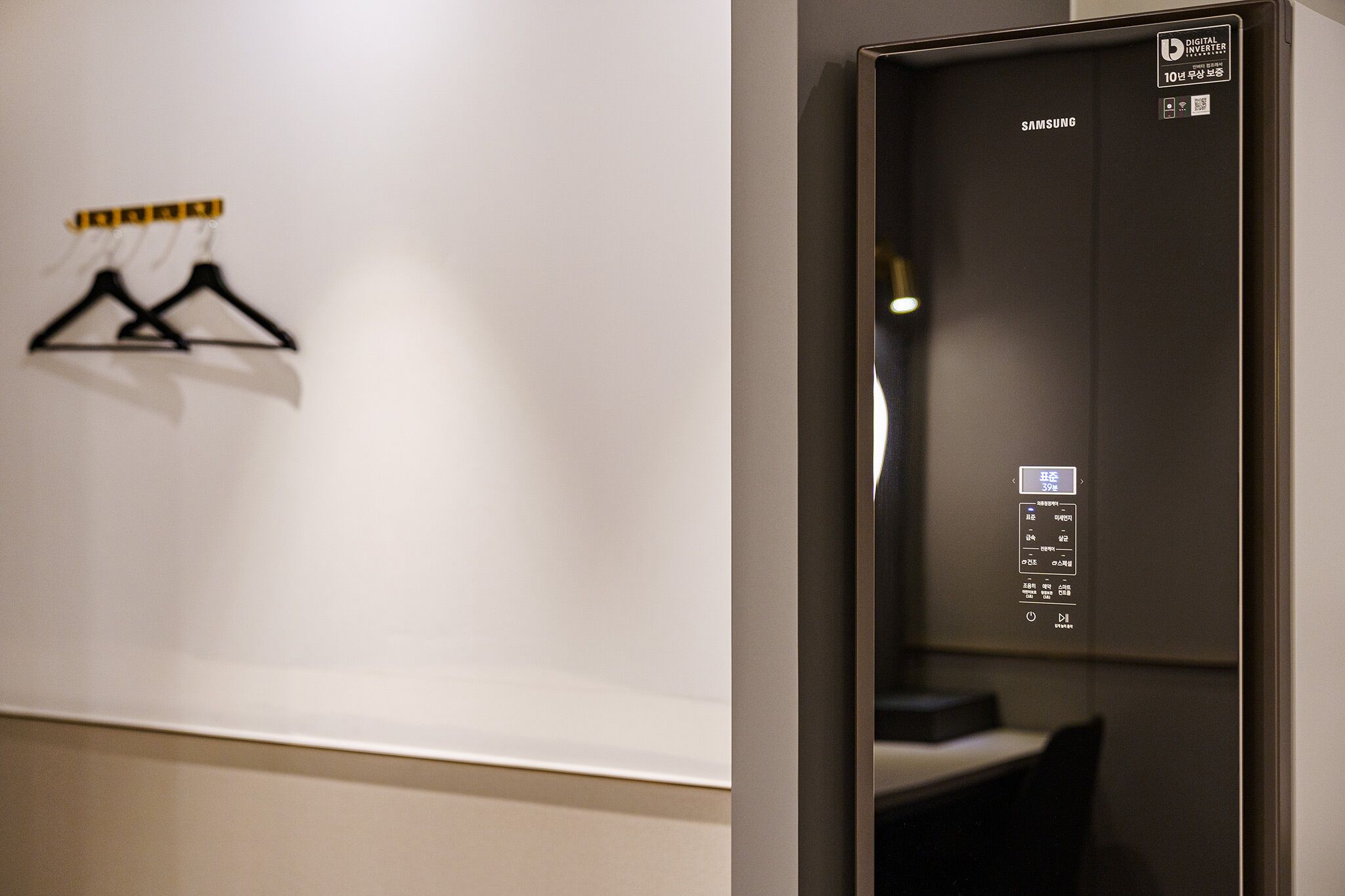 A digital elevator with a Samsung logo, a wall-mounted coat rack, and a digital display with room information.