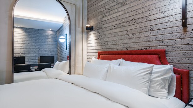 Ein Hotelzimmer mit einer ziegelmusterigen Wand, einem roten, gepolsterten Kopfteil und einem großen Bett mit weißer Bettwäsche.