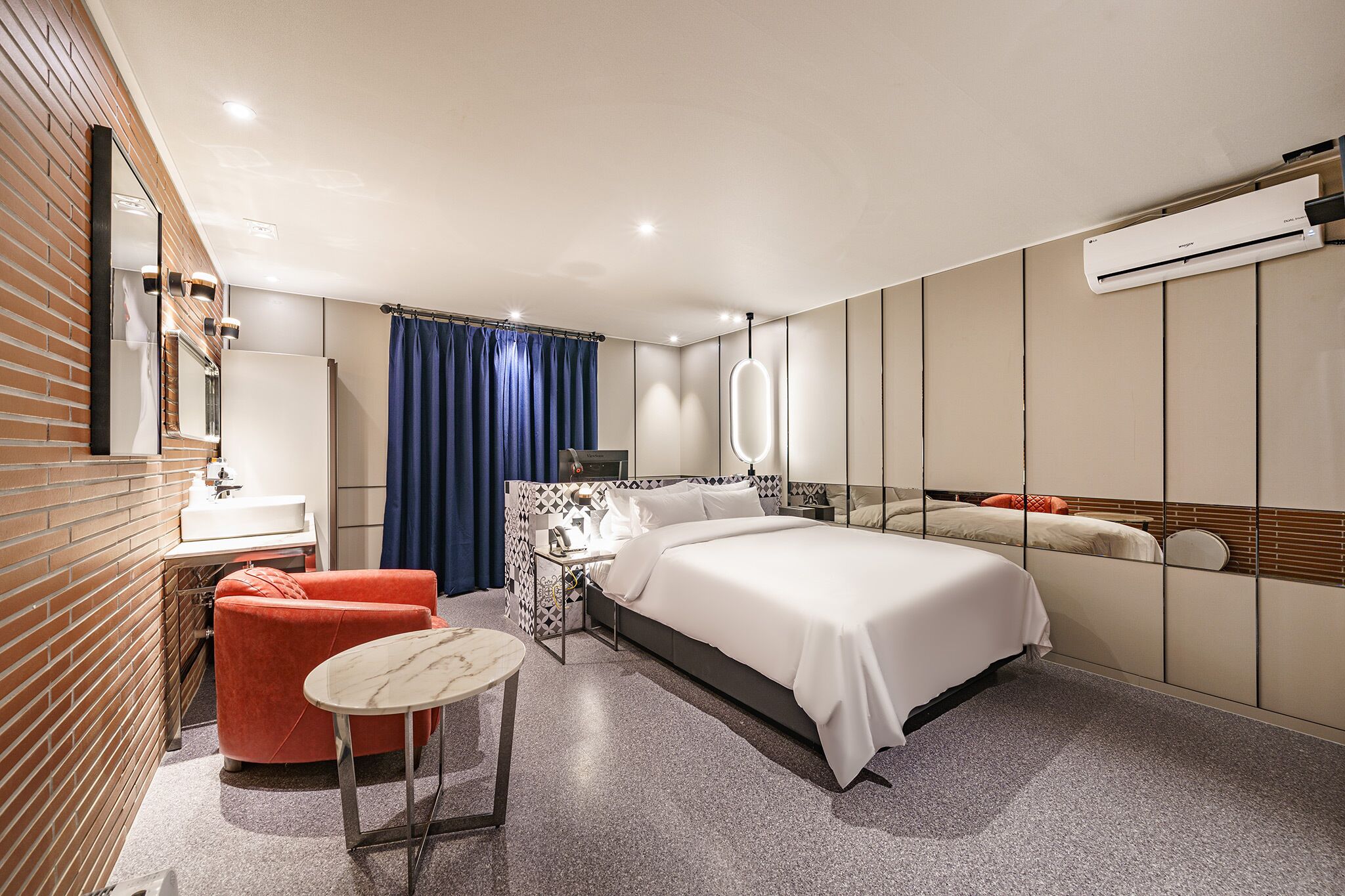 Ein modernes Hotelzimmer mit Bett, kleinem Tisch, Stuhl, Schminktisch mit Spiegel und Klimaanlage.