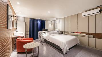 Ein modernes Hotelzimmer mit Bett, kleinem Tisch, Stuhl, Schminktisch mit Spiegel und Klimaanlage.